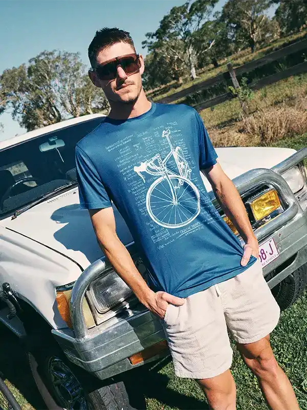 Man wearing blue cycling t-shirt with bicycle blueprint design, standing by white truck outdoors