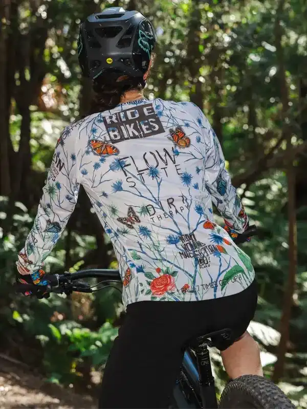 Woman riding mountain bike in forest wearing floral long sleeve cycling jersey with butterfly print