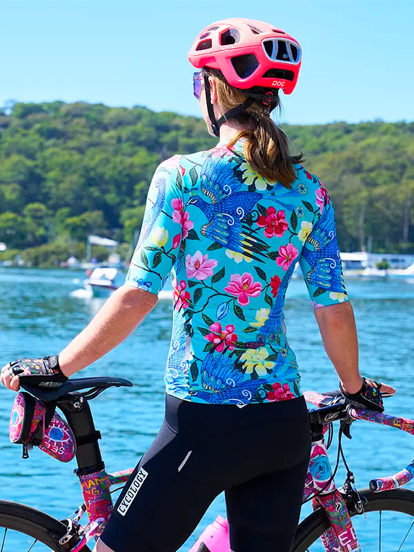 Person wearing a colorful cycling jersey and helmet by a lake