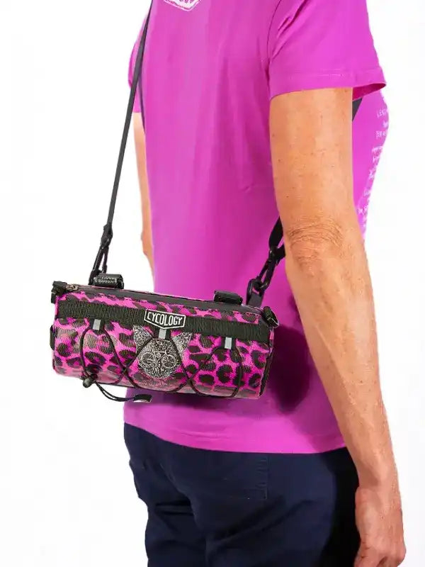 Pink leopard print cycling bag with black straps, worn crossbody by person in magenta tee