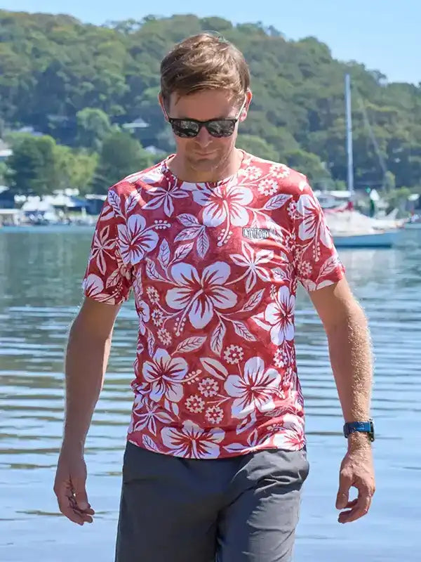 Man wearing red floral cycling shirt by water, sunglasses, gray shorts, outdoor active wear