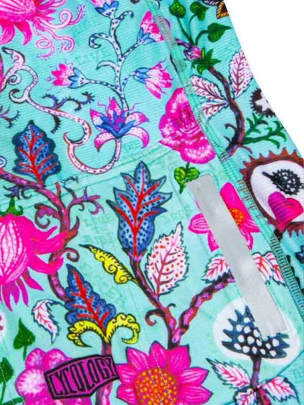 Vibrant floral cycling shorts with pink, blue, and green botanical print, featuring a rear pocket and brand patch.