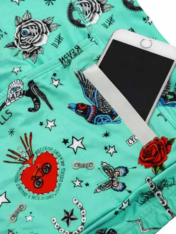 Mint green cycling shorts with tattoo-style roses, stars, and bike graphics, featuring phone pocket