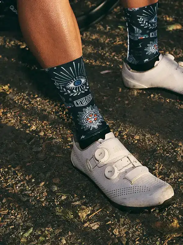 Cycling socks with eye and sunburst design, worn with white clip-in shoes on dirt trail