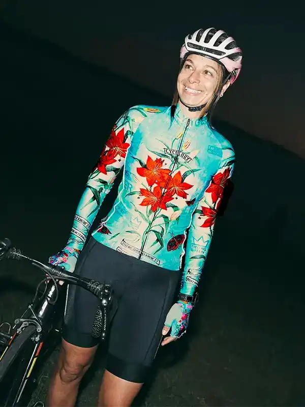 Woman in floral cycling jersey and helmet, standing with bike at dusk