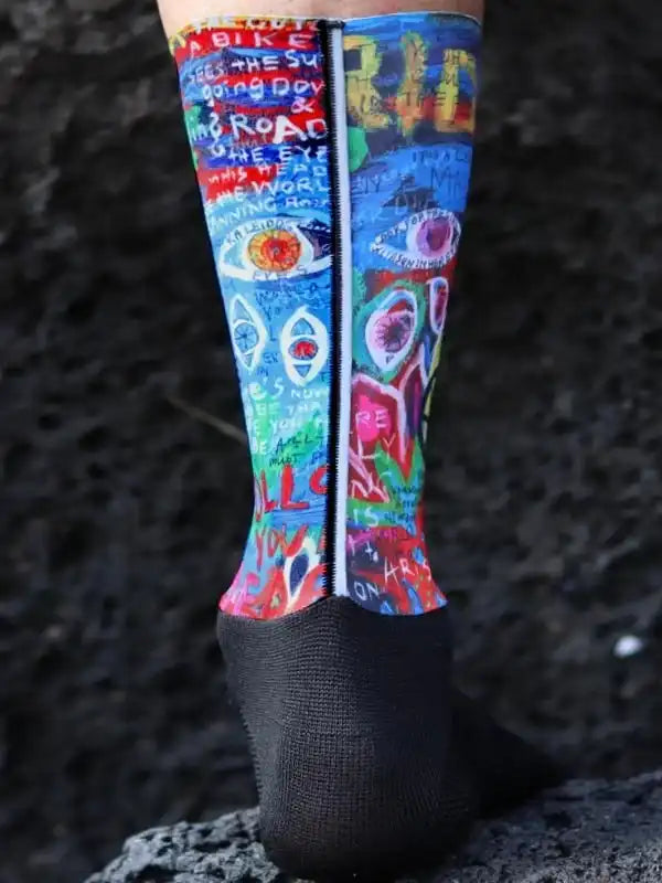 Colorful cycling socks with graffiti art and eye designs, worn on rocky terrain