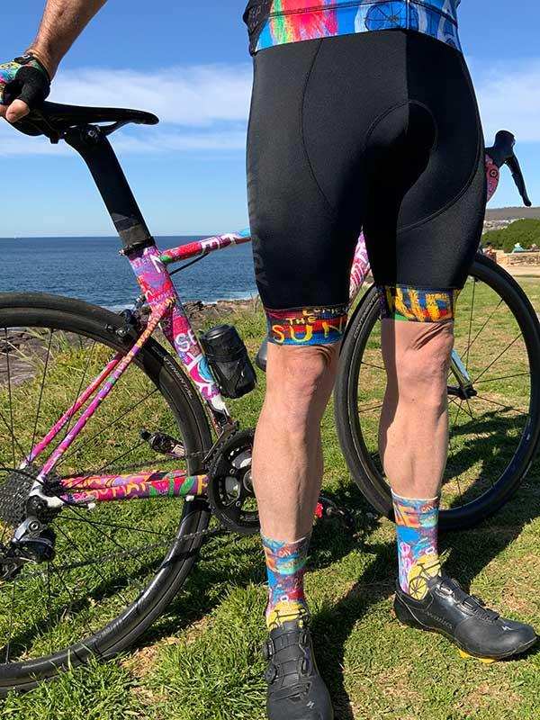 Colorful cycling shorts and socks with vibrant patterns, paired with a matching bike, outdoors by the sea.