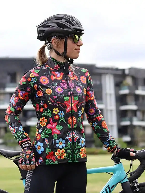 Woman in colorful floral cycling jersey and helmet, standing with road bike outdoors