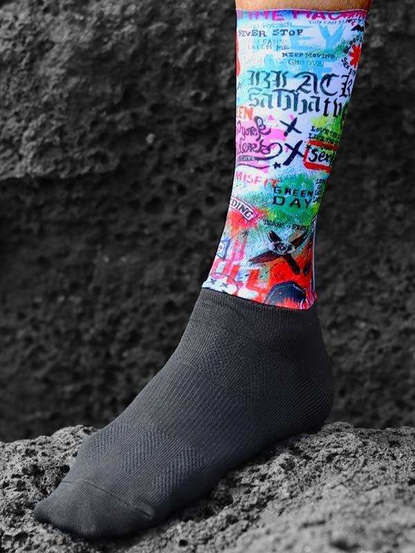 Colorful graphic cycling socks with band names, worn on foot against rocky background