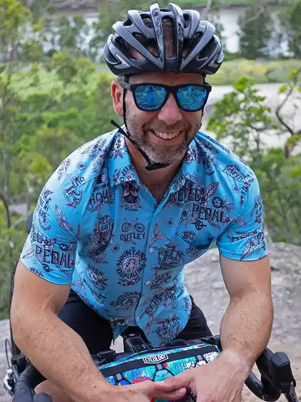 Man cycling in blue patterned jersey, helmet, and sunglasses outdoors