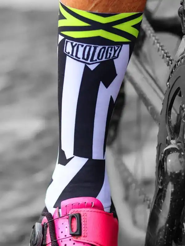 Cycling socks with bold black, white, and neon yellow design, worn with pink cycling shoes near bike chain