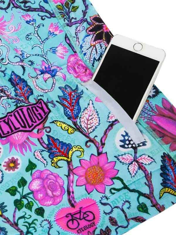 Vibrant floral cycling shorts with phone pocket, featuring bold pink blooms and bike logo on teal fabric.