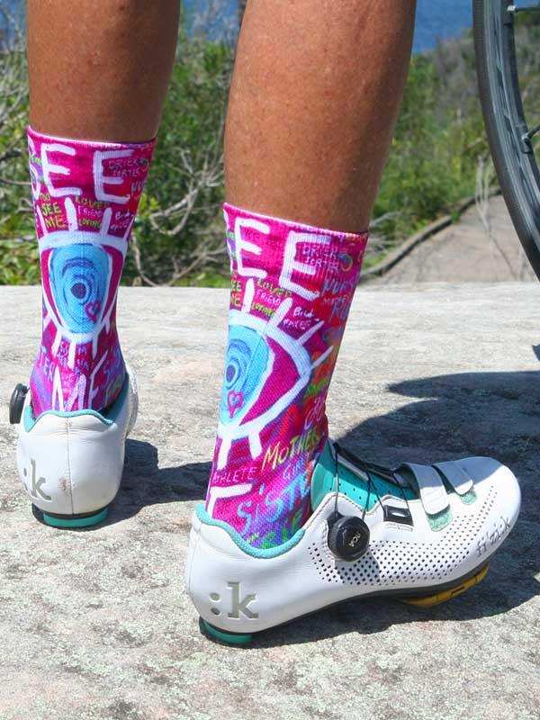 Vibrant pink cycling socks with bold graphic design, worn with white bike shoes on rocky trail