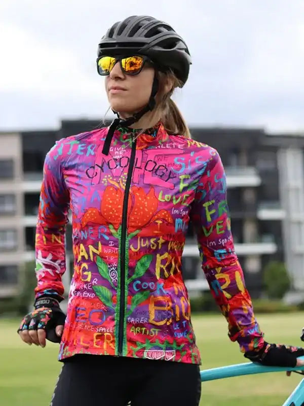Woman in vibrant cycling jersey with colorful graffiti-style print, wearing helmet and sunglasses outdoors