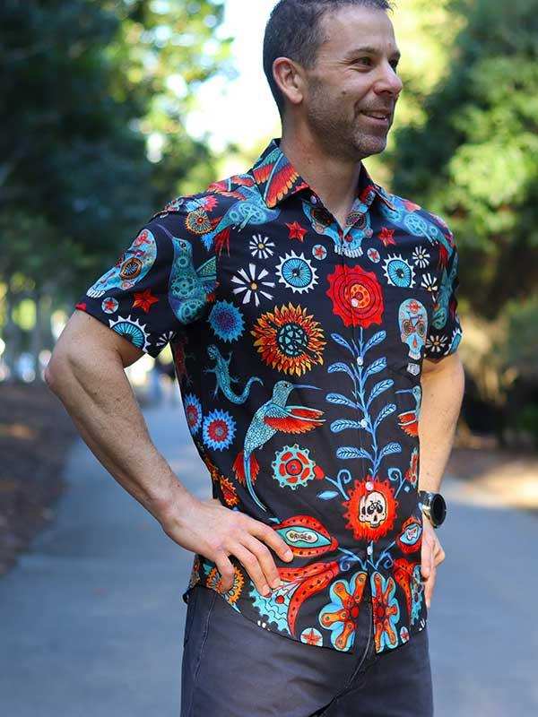 Men's colorful floral cycling shirt with skull and hummingbird print, worn outdoors on a sunny path