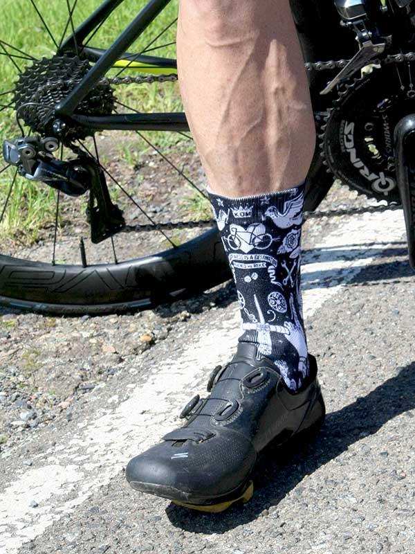 Cycling socks with bike graphics worn with black cycling shoes, next to road bike on pavement