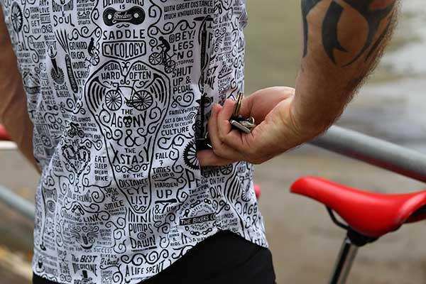 Men's cycling jersey with bold graphic print, featuring cycling phrases and bike motifs, worn by rider near red saddle.