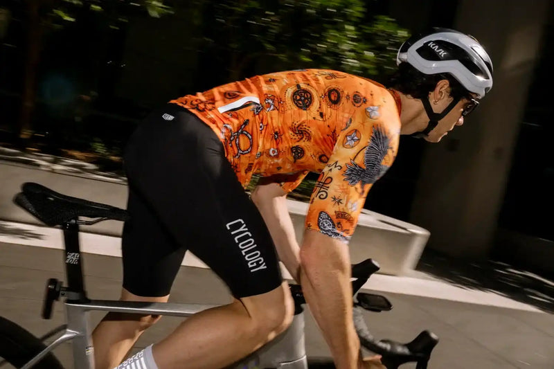 Man cycling in vibrant orange patterned jersey and black Cycology shorts, wearing Kask helmet