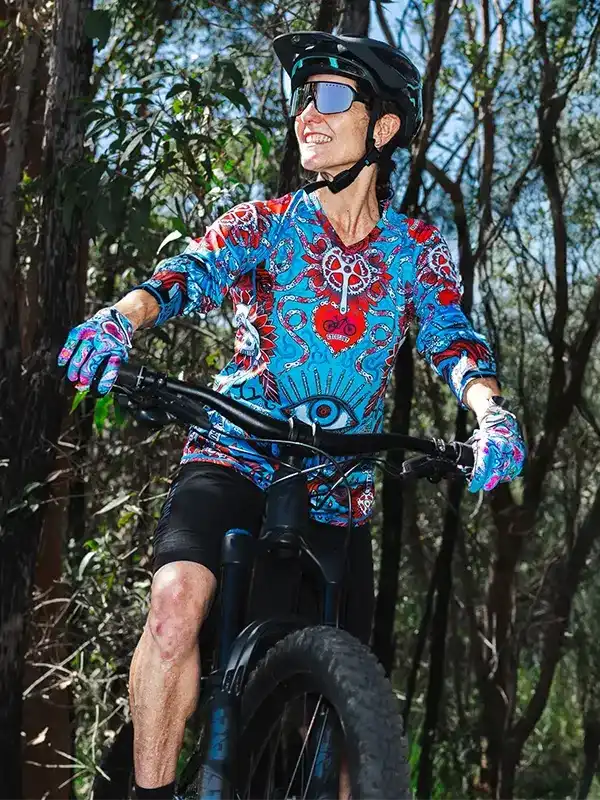 Woman riding mountain bike in vibrant cycling jersey with eye and heart print, forest trail