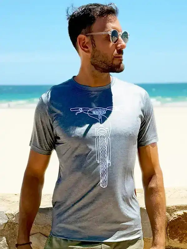 Man wearing gray cycling t-shirt with white bike graphic, beach background, sunglasses, casual outdoor style