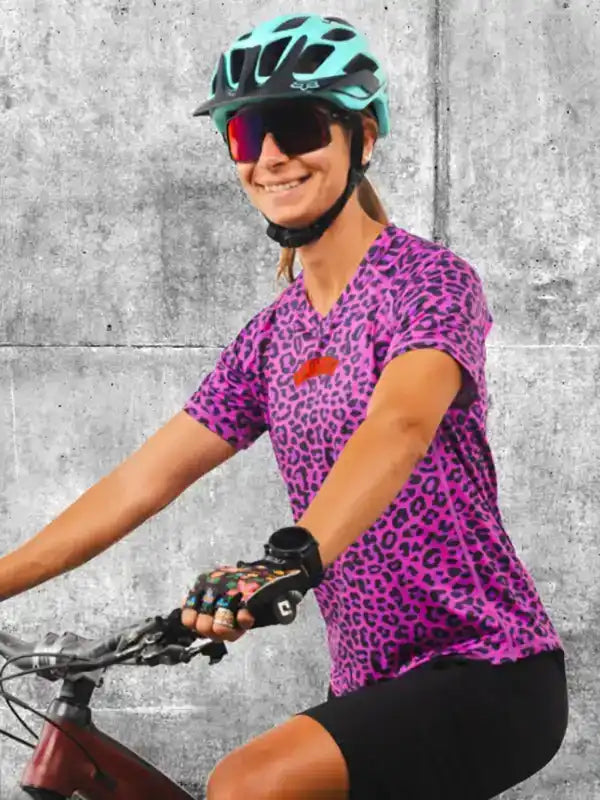 Woman cycling in vibrant pink leopard print jersey, helmet, and sunglasses