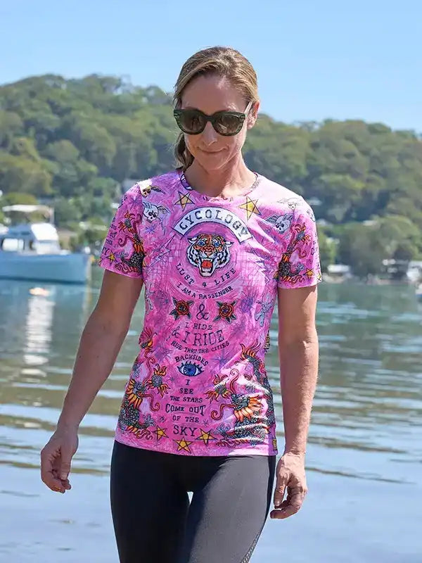 Woman wearing vibrant pink cycling shirt with tiger and star designs near waterfront