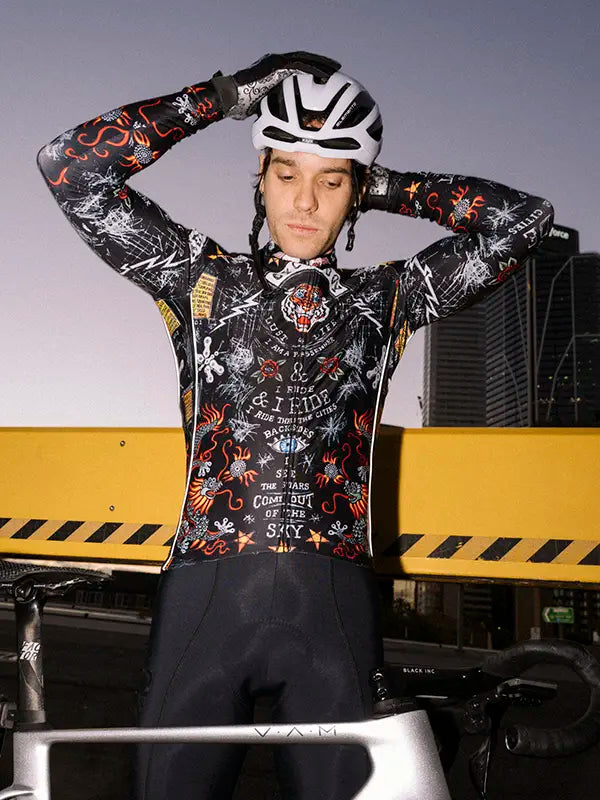 Person wearing a black long sleeve cycling jersey with a helmet, standing in front of a yellow and black striped barrier.