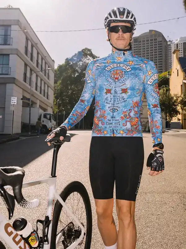 Man in blue patterned cycling jersey and black shorts standing with road bike in urban setting