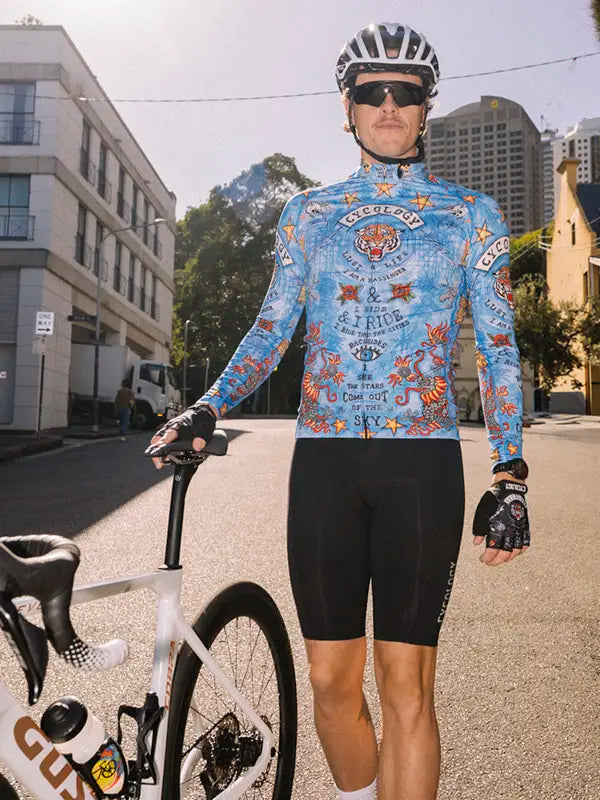 Cyclist in a colorful jersey and black shorts standing next to a bicycle on a city street.