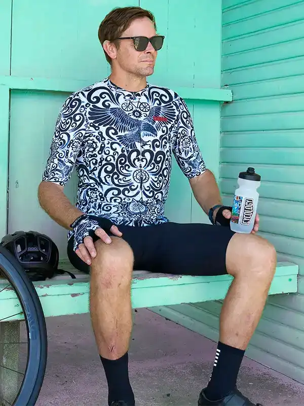 Man in black and white patterned cycling jersey and shorts, holding water bottle, seated on mint bench