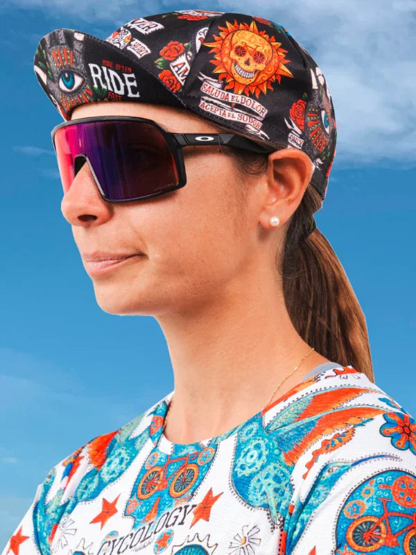 Woman wearing vibrant cycling cap and sunglasses with bold graphic jersey, ideal for road bike rides under sunny skies.