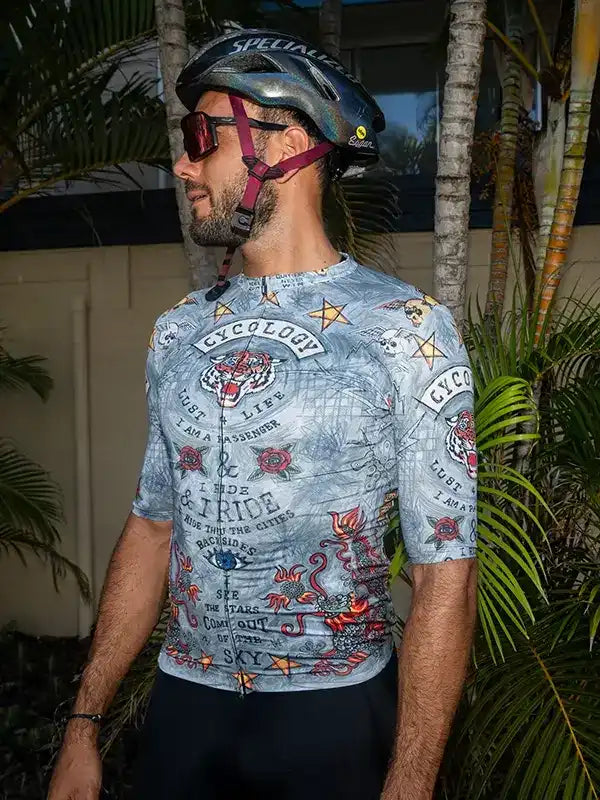 Men's cycling jersey with bold tattoo-style graphics, worn with helmet and sunglasses outdoors