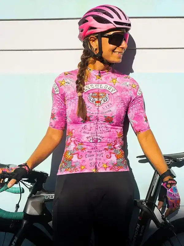 Woman in pink tattoo-style cycling jersey and helmet, standing with road bike, ready to ride.