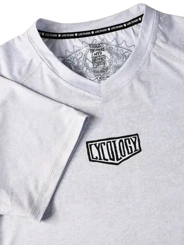 White cycling jersey with 'CYCOLOGY' logo, breathable fabric, and 'LIVE TO RIDE' tag detail