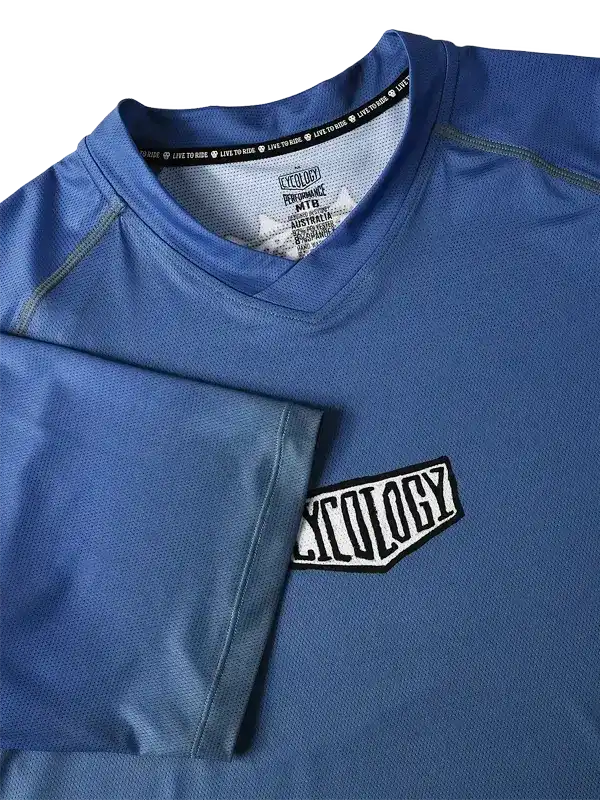 Blue cycling jersey with 'Cycology' chest patch and performance tag, ideal for men's and women's rides