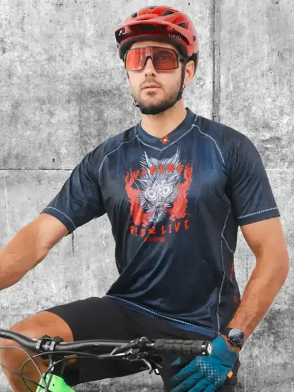 Man in cycling jersey with owl graphic, red helmet, and sunglasses on bike against concrete wall