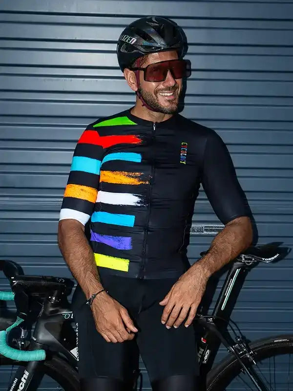 Man in colorful striped cycling jersey and helmet, standing with road bike against blue garage door