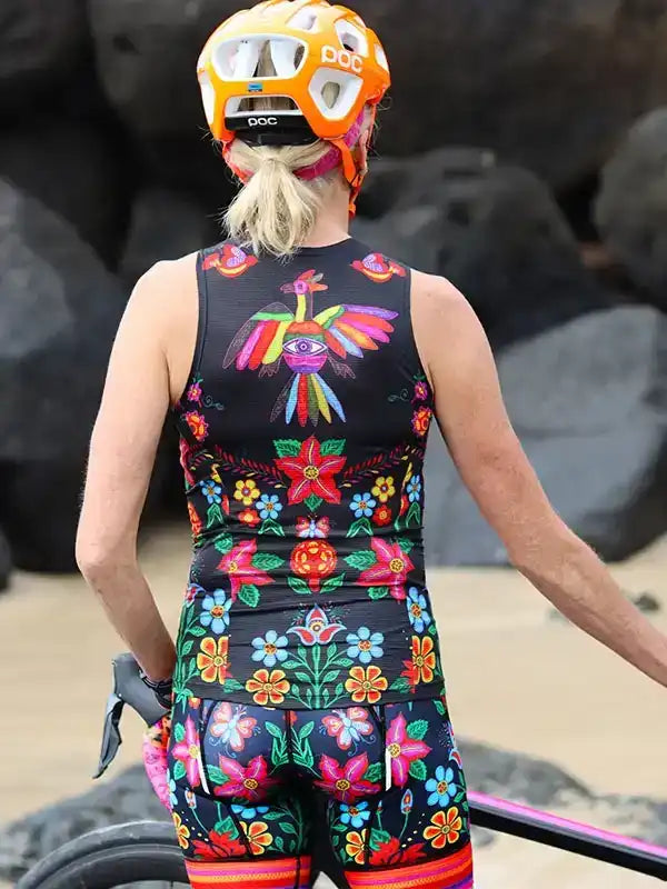 Woman in colorful floral cycling jersey and shorts, wearing POC helmet, standing by bike near rocks