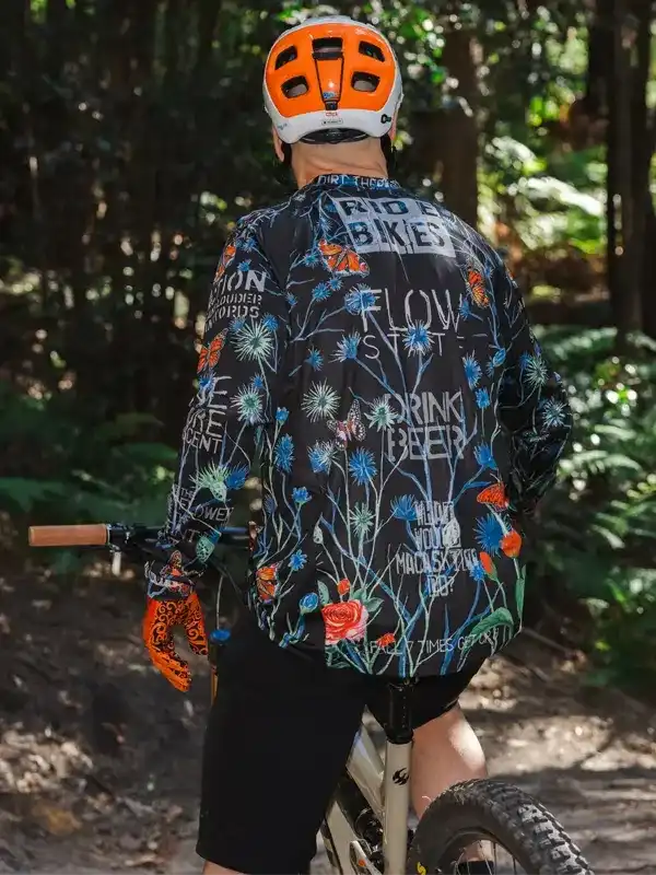 Men's cycling jersey with floral print and bold text, worn on forest trail ride