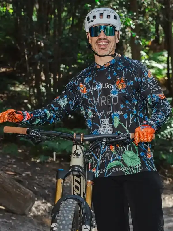 Man in floral cycling jersey and helmet on mountain bike in forest trail