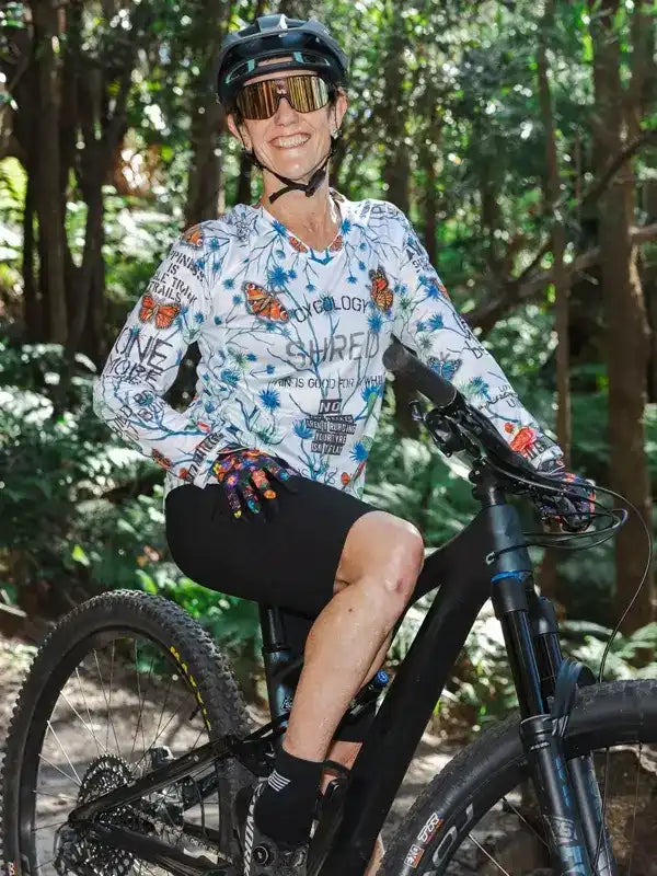Woman in butterfly-print cycling jersey and helmet riding mountain bike through forest trail