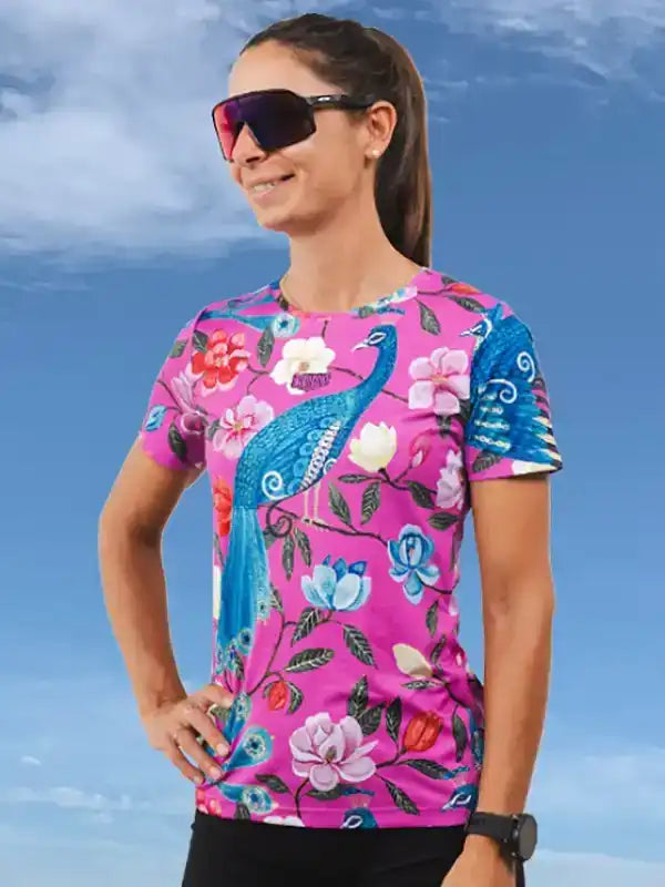 Woman wearing vibrant pink cycling jersey with peacock and floral print, ideal for women's cycling apparel