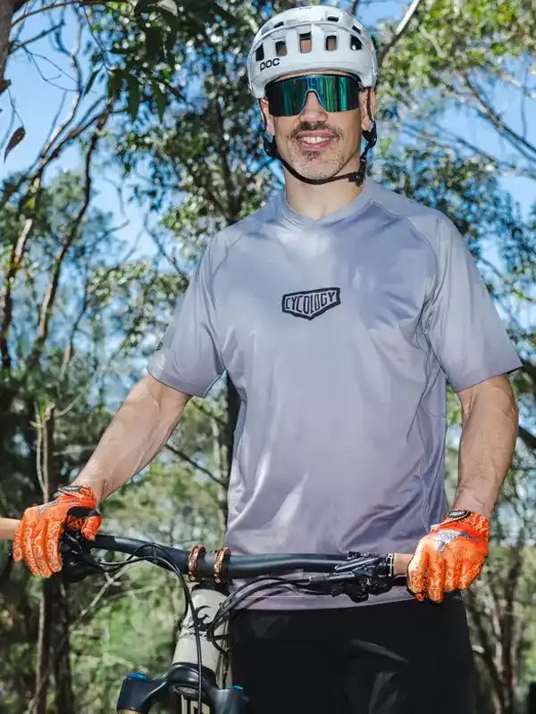 Man wearing gray cycling jersey and orange gloves, riding bike in forest