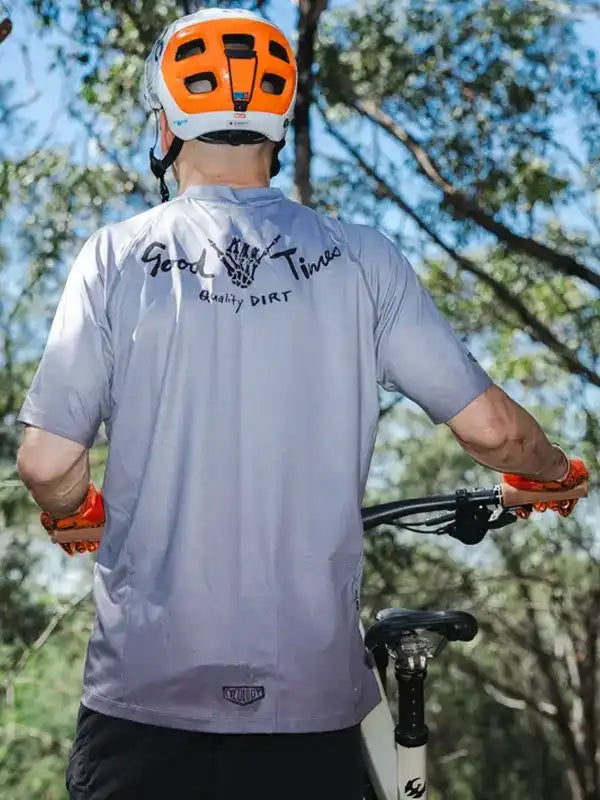 Cyclist wearing gray 'Good Times Quality Dirt' jersey with orange helmet and gloves, outdoors