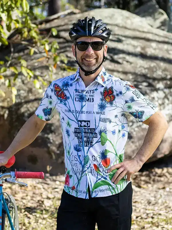 Man wearing butterfly print cycling jersey with helmet, standing beside bike outdoors
