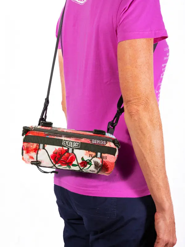 Person wearing a pink shirt with a floral-patterned bag over their shoulder on a white background