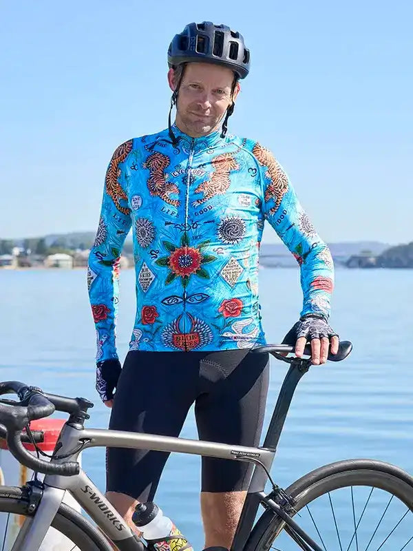 Man in vibrant blue patterned cycling jersey and black shorts, standing with road bike by water