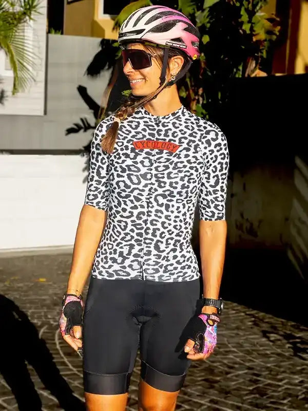 Woman in leopard print cycling jersey and black shorts, wearing pink helmet and sunglasses