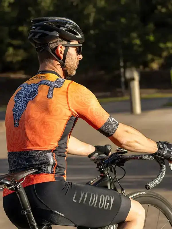 Man cycling in orange and black cycling jersey with graphic design, wearing helmet and sunglasses