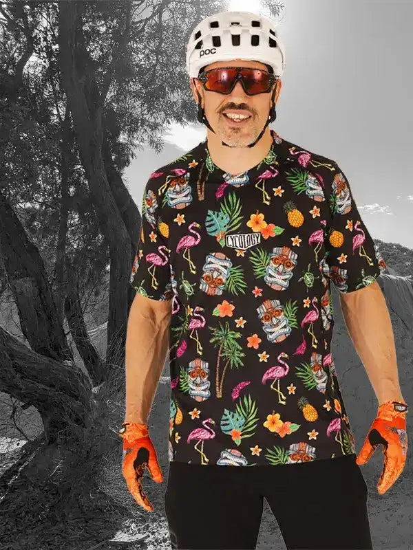 Man wearing tropical print cycling jersey with flamingos, pineapples, and tiki masks, helmet, and gloves
